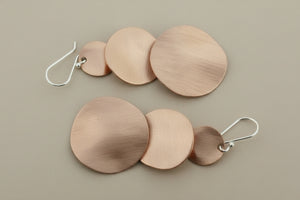 Pair of copper round earrings on a dark gray background