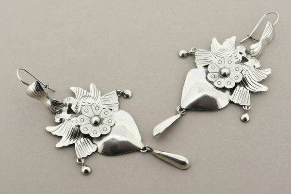Pair of silver earrings with floral designs on a gray background