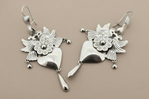 Pair of silver earrings with floral designs on a gray background