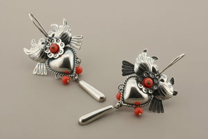 Pair of silver earrings with red heart and bead details on a gray background