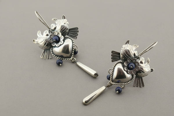 Pair of silver heart-shaped earrings with blue gemstones on a gray background