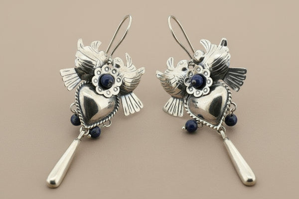 Pair of silver heart-shaped earrings with blue stones on a gray background