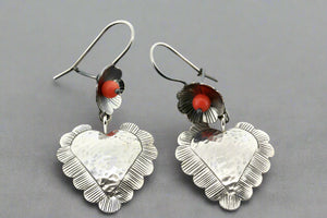 Pair of silver heart-shaped earrings with orange beads on a gray background