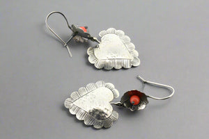 Pair of silver heart-shaped earrings with orange stones on a gray background
