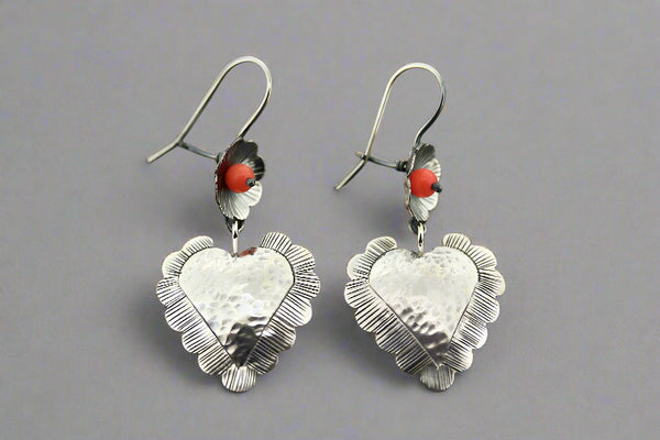 Silver heart-shaped earrings with red beads on a gray background