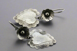 Pair of silver leaf-shaped earrings with black accents on a gray background