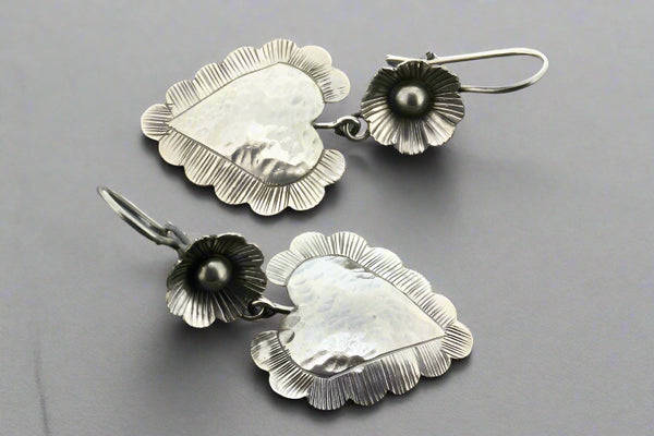 Silver heart-shaped earrings with floral details on a gray background