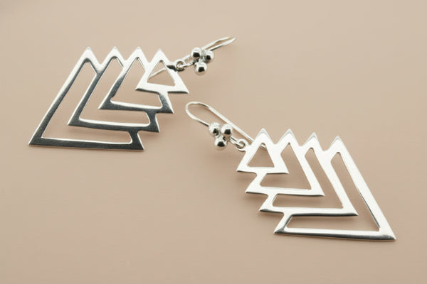 Silver geometric earrings on a dark gray background