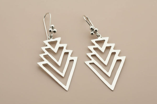 Pair of silver geometric earrings on a dark gray background
