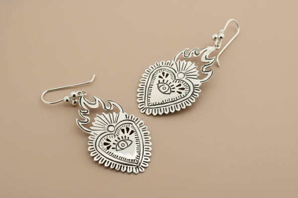 Silver heart-shaped earrings with intricate designs on a dark gray background