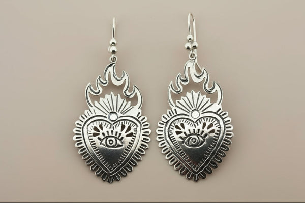 Silver heart-shaped earrings with flame designs on a gray background