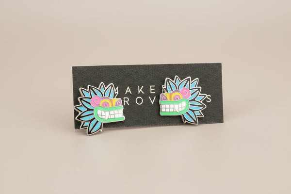 Pair of colorful mask-shaped earrings on a black card with 'MAKER ROW' branding.