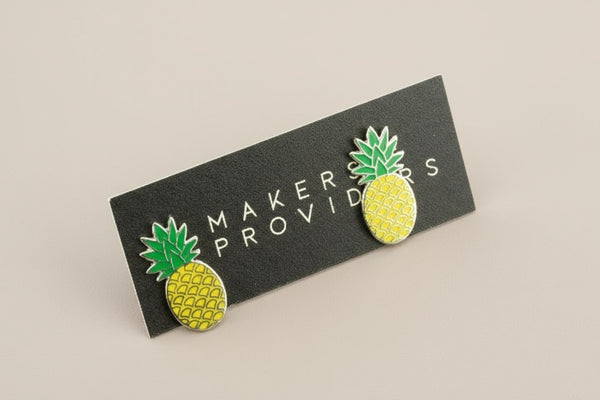 Pineapple-shaped earrings on a 'Makers & Providers' card against a gray background