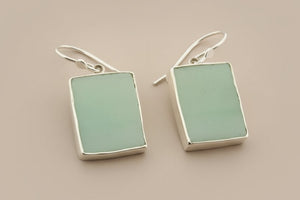 Pair of earrings with rectangular green stones on a gray background