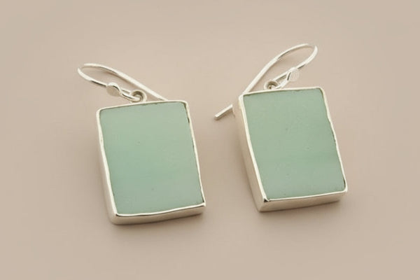 Pair of earrings with rectangular green stones on a gray background