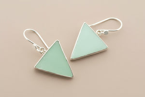 Pair of triangle-shaped earrings with green stones on a gray background