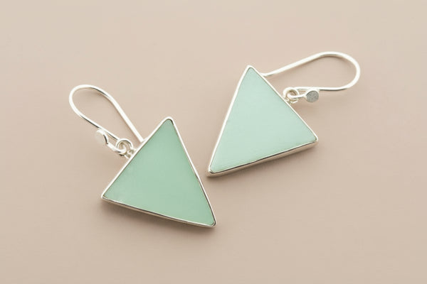 Pair of triangle-shaped earrings with green stones on a gray background