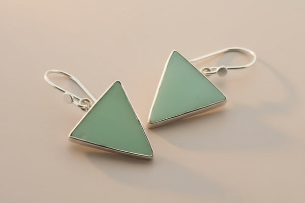 Pair of triangle-shaped earrings with light green stones on a gray background