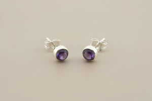 Pair of silver earrings with purple gemstones on a gray background