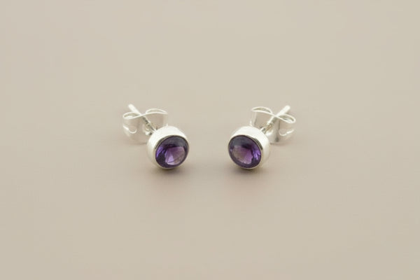 Pair of silver earrings with purple gemstones on a gray background
