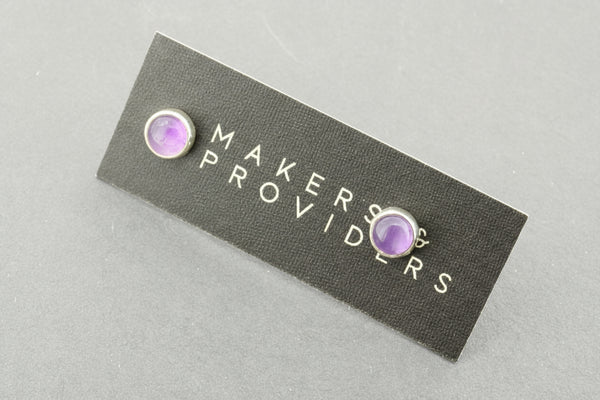 Pair of earrings with purple gemstones on a 'Maker Providers' card against a gray background