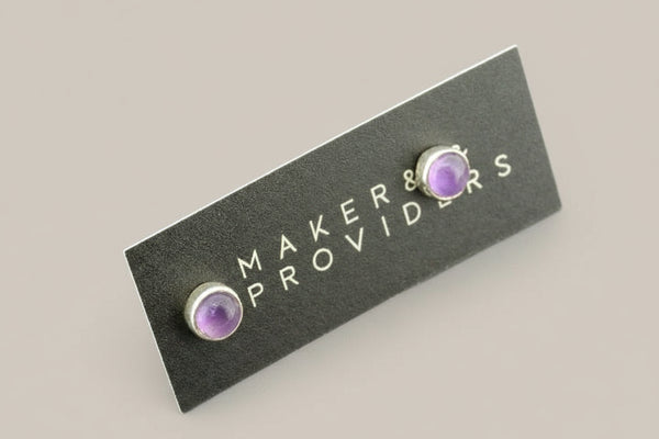Pair of purple gemstone earrings on a 'MAKERS PROVIDERS' card against a gray background
