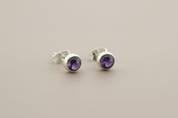 Pair of silver stud earrings with purple gemstones on a gray background