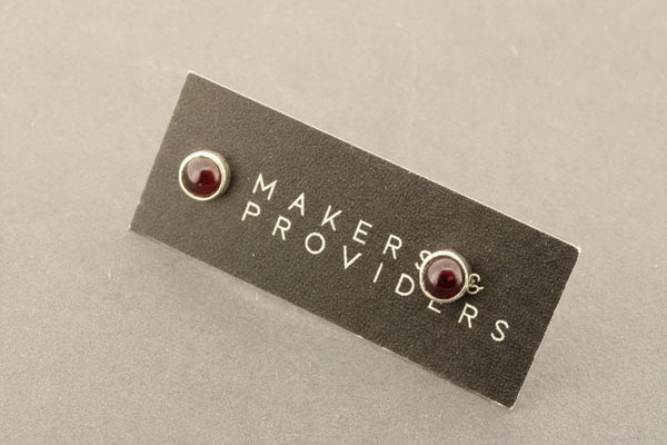 Pair of silver earrings with red gemstones on a 'Makers & Providers' card.