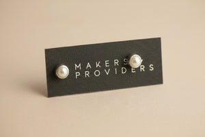 Pair of pearl earrings on a 'MAKERS PROVIDERS' card against a gray background