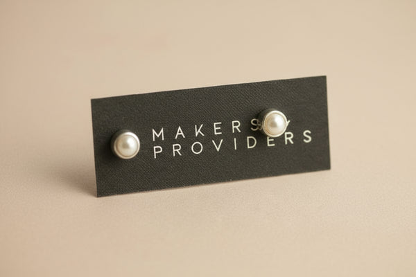 Pair of pearl earrings on a 'MAKERS PROVIDERS' card against a gray background