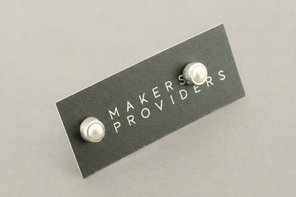 Pair of pearl earrings on a 'MAKERS PROVIDERS' card against a gray background