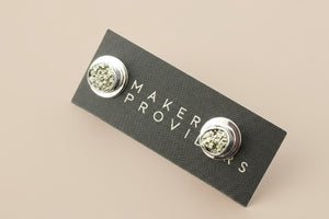 Silver earrings on a 'Maker Provisions' card against a gray background