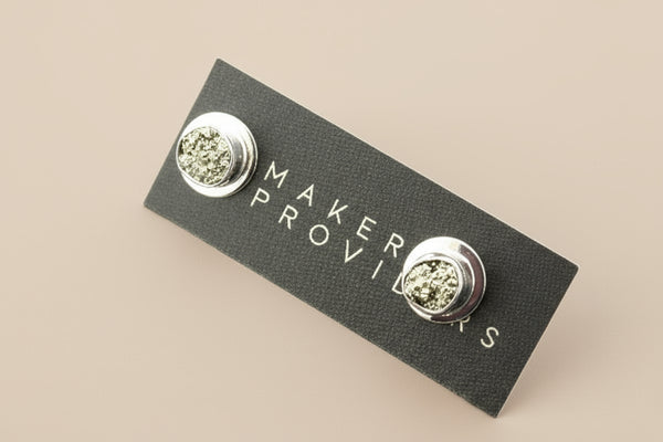 Silver earrings on a 'Maker Provisions' card against a gray background