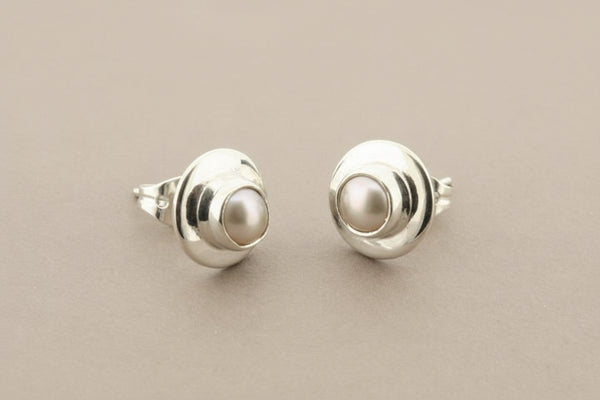 Pair of silver stud earrings with pearl centers on a gray background