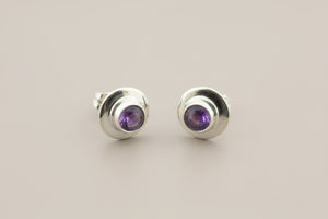 Pair of silver stud earrings with purple gemstones on a gray background