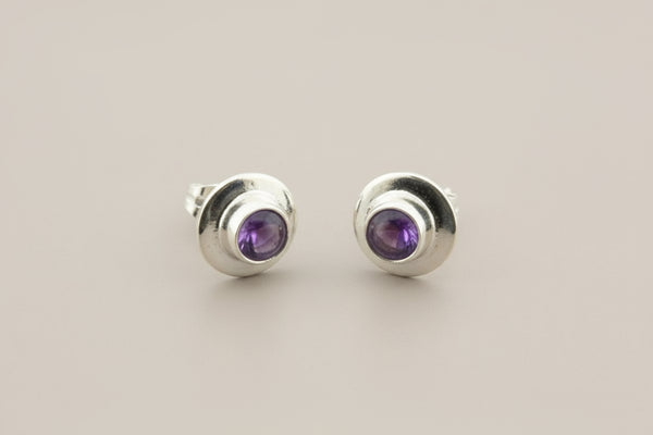 Pair of silver stud earrings with purple gemstones on a gray background