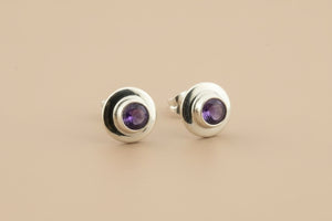Silver stud earrings with purple gemstones on a gray background