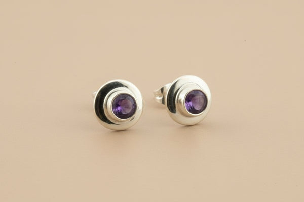 Silver stud earrings with purple gemstones on a gray background