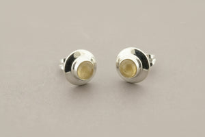 Pair of silver stud earrings with a yellow gemstone on a gray background