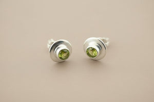 Pair of silver stud earrings with green gemstones on a gray background
