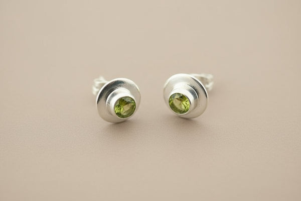 Pair of silver stud earrings with green gemstones on a gray background