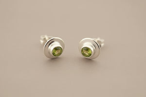 Pair of silver stud earrings with green gemstones on a gray background