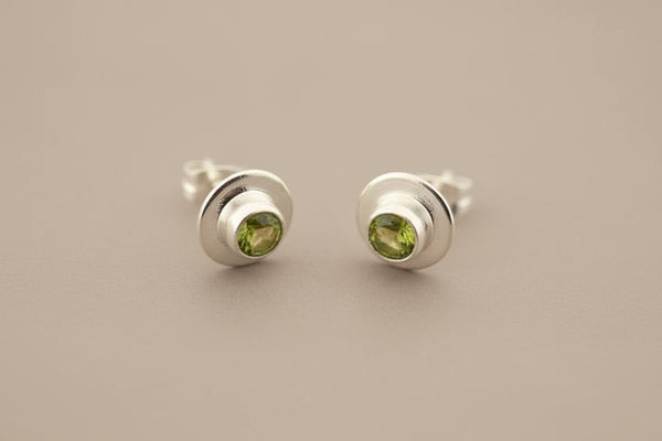 Pair of silver stud earrings with green gemstones on a gray background