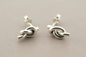 Pair of silver knot earrings on a gray background