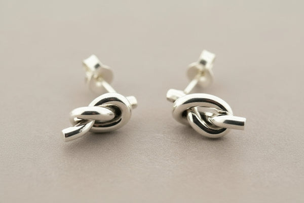 Pair of silver knot earrings on a gray background