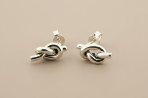 Pair of silver knot earrings on a gray background