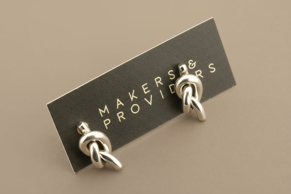 Pair of silver knot earrings on a 'Makers & Providers' card against a gray background