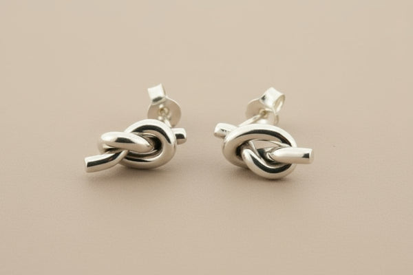 Pair of silver knot earrings on a gray background