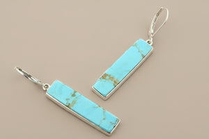 Turquoise bar earrings with silver hooks on a gray background