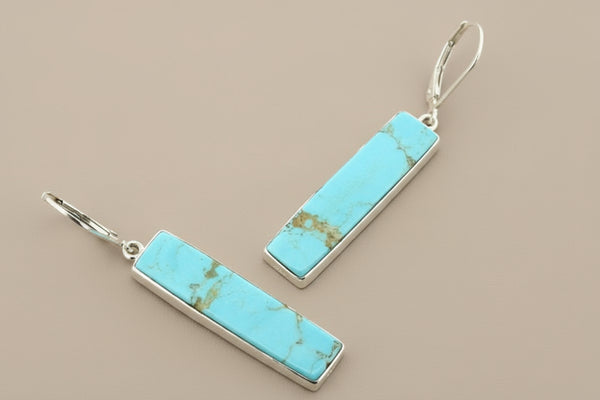 Turquoise bar earrings with silver hooks on a gray background